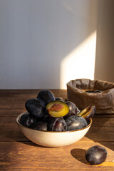 dark blue plum in a plate on a wooden table in the morning sun