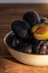 dark blue plum in a plate on a wooden table in the morning sun