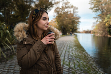 A pretty caucasian woman smiling while holding a coffee and enjoying a walk at park. Copy space