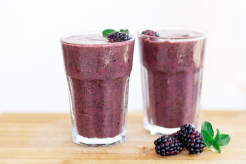 Delicious blackberry smoothie with mint and fresh berries in glasses on wood desk and white background