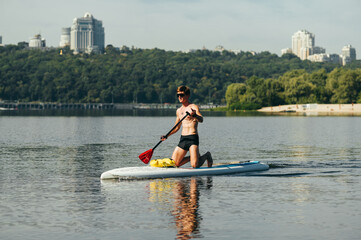 Athletic young man actively spends time on the water, swims on a sup board, paddles and looks away....