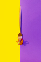 metalic fork with jelly worms on a vertical yellow and purple color block background