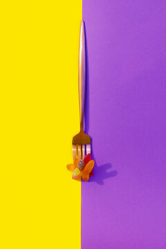 Metalic Fork With Jelly Worms On A Vertical Yellow And Purple Color Block Background