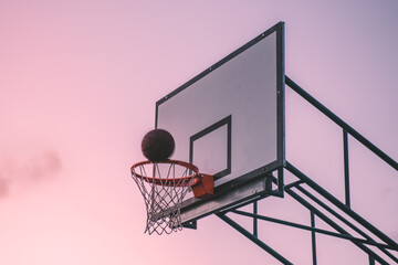 Basketball hoop with ball scoring going through at sunset sky. Basketball board isolated 