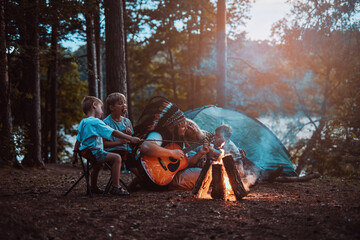 American mother and father having a good time and resting in forest with their children which cooking treats on campfire.