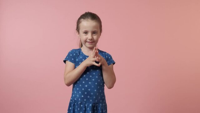 A beautiful cute girl put her hands together and asks for something. Blue dress with polka dots. The girl has long hair. Pink background.