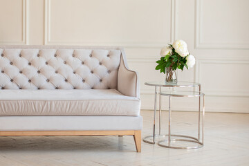 Modern Spacious minimalistic living room interior with a gray sofa and a coffee table with a vase with a bouquet of peonies flowers against a white wall. Scandinavian  interior home. Cozy room decor.
