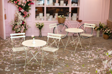 Empty cafe terrace with white table and chair. Pink exterior of the cafe restaurant. interior Street cafe. Cozy street with flowers and French-style cafe table. Decor facade of coffeehouse with bike. 