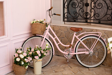 Fototapeta na wymiar Vintage bike with basket with bouquet flowers of roses stands near cafe of bakery. Eco transport. pink bicycle with flower pots with roses stands on street coffee shop. wedding decorations. 