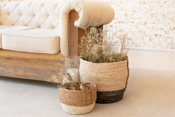 Wicker baskets with dried flowersnear the sofa on floor. Living room hygge, autumn cozy home decor....