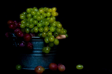 Green and violet grapes lie in a metal bowl against a black background. Tasty fresh grapes on a black background. Poster for the kitchen. Kitchen interior. Fruits for salad. Fresh