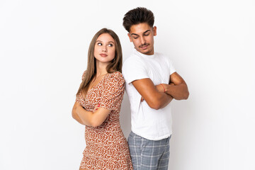 Young caucasian couple isolated on white background keeping the arms crossed looking at each other