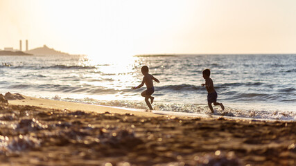 Fototapeta na wymiar Silhouette of little boys playing at the beach during sunset, beautiful bokeh on sand