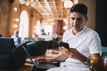 Young man chatting on smartphone and using laptop in restaurant