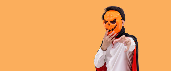 Asian man wearing Halloween costume as vampire Dracula on orange background, wearing pumpkin mask,...