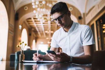 Focused young man working with planner and mobile phone in cafe