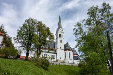 Fototapeta na wymiar Old white Saint Martin Church in Bled, Slovenia hidden behind trees