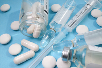 white pills and capsule are scattered on a blue background. close-up of a syringe of ampoules and a glass jar of medicine. virus protection