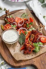 roasted chicken wings with paprika, white sauce and vegetables on wooden board on the table
