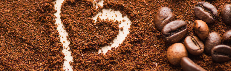 close up view of heart drawn on ground coffee near beans, panoramic shot