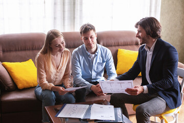 Fototapeta premium Confident realtor showing house plan to couple of potential buyers indoors