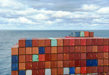 Fully loaded container ship sailing through a blue, calm ocean. View on the stack of the containers...