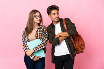 Young student couple isolated on white background looking up while smiling