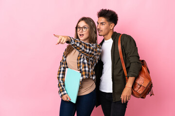 Young student couple isolated on white background pointing to the side to present a product