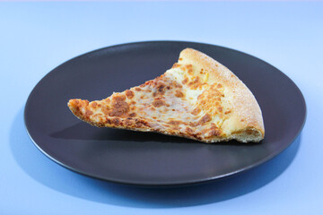 Dried slice of pizza on a black table on a blue background. Food concept.