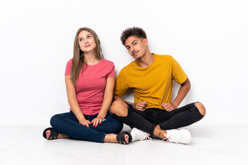 Fototapeta na wymiar Young couple sitting on the floor isolated on white background posing with arms at hip and smiling