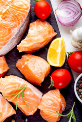 Fresh raw salmon fillet on black cutting board with lemon and spices. Healthy food concept. Close up view
