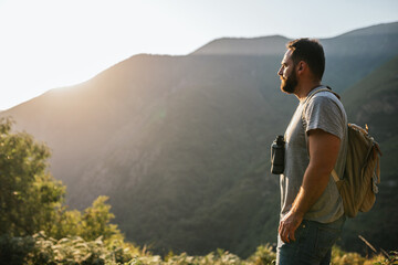 young man looking through binoculars on a mountain at sunset