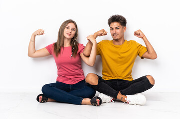 Fototapeta na wymiar Young couple sitting on the floor isolated on white background doing strong gesture