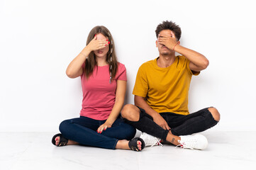 Fototapeta na wymiar Young couple sitting on the floor isolated on white background covering eyes by hands. Do not want to see something
