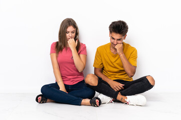 Fototapeta na wymiar Young couple sitting on the floor isolated on white background having doubts
