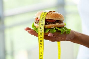 Diet concept, woman holding harmful fat burger with yellow measuring tape