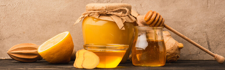 sweet honey, ginger root and lemon on wooden surface near beige concrete wall, panoramic shot