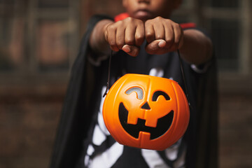 Unrecognizable boy wearing modern Halloween costume demonstrating plastic Jack O' Lantern basket...