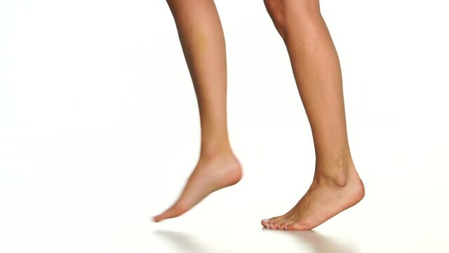 female bare feet walk on toes from left to right on a white background