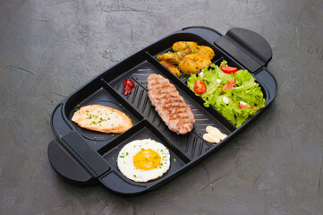 Breakfast, fried steak or cutlet, salad with tomato and green vegetables, toast, potatoes, egg on black plate. The concept of a healthy diet, diet, menu, high-grade lunch