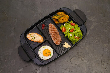 Breakfast, fried steak or cutlet, salad with tomato and green vegetables, croutons, potatoes, egg , view from the top, dark background. Concept healthy eating, diet, menu, nutritious food.