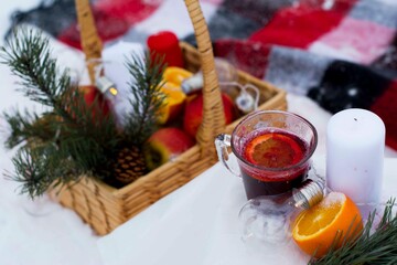 Winter picnic in the forest. On the table we see a cup of mulled wine to keep warm after a walk in the snowy forest. Mulled wine with orange. Against the background is a basket with spruce branches.