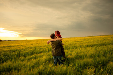 Naklejka na ściany i meble Young couple in a wheat field at sunset. Couple spend romantic time together.