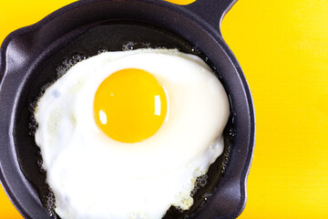 Fried egg. Close up view of the fried egg on a frying pan on yellow background.