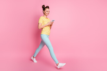 Fototapeta na wymiar Full length profile photo of attractive lady funny buns hold telephone hands writing new blog post walk street wear casual striped t-shirt pants footwear isolated pink color background