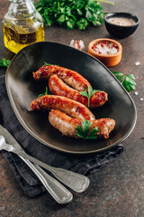 Grilled sausage with greens on black plate over dark background.