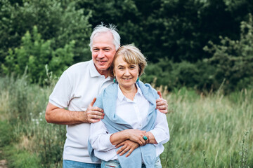 mature couple is walking with dog in park. Elderly couple resting in nature with a dog. Full-length portrait of an elderly man and woman in white shirts and jeans. Stylish and modern grandparents.