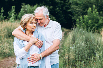 mature couple is walking with dog in park. Elderly couple resting in nature with a dog. Full-length portrait of an elderly man and woman in white shirts and jeans. Stylish and modern grandparents.