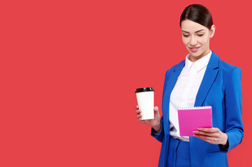 Confident business woman in blue suit with cup of tea or coffee holding notebook in red isolated background