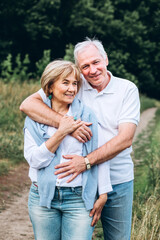 mature couple is walking with dog in park. Elderly couple resting in nature with a dog. Full-length portrait of an elderly man and woman in white shirts and jeans. Stylish and modern grandparents.